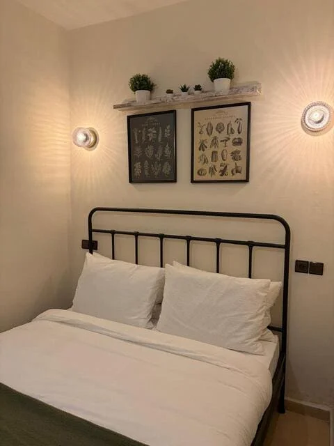 Simple double room with white linen, a black metal bed and botanical prints on a wall shelf